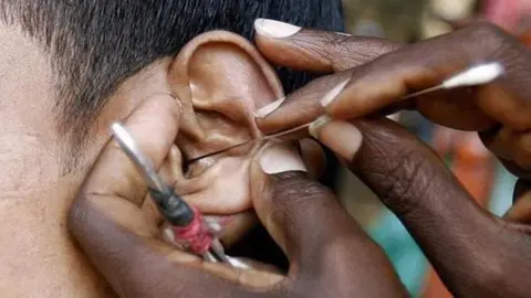 A close-up of a man's ear being cleaned of earwax using a long thin implement