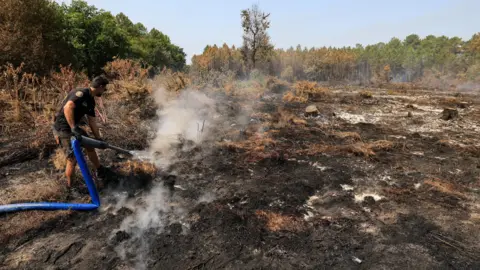 Reuters A volunteer sprays water in a burnt forest area