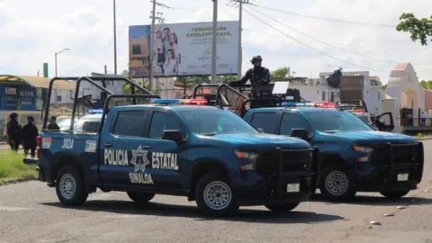 REUTERS/Jesus Bustamante Two trucks emblazoned with the words Sinaloa State Police block a road in Culiacan in this file photo from 11 September 11, 2024. 