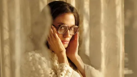 Studio Canal Angelina Jolie successful  Maria, wearing a achromatic  knitted sweater and glasses, looking astatine  the camera