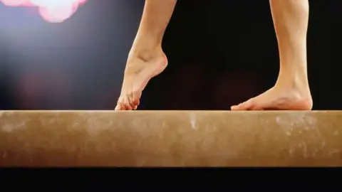 Only the feet of a gymnast can be seen as she poses on the beam 