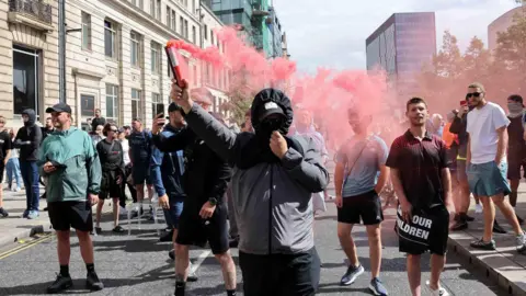 Reuters A protester with a hood up and hiding his face holds up a red smoking flare in Liverpool