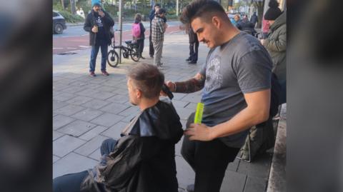 Eddie giving a man a haircut outside on the street