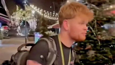 Young man with rucksack on looks at the camera and says 'I actually don't know how we are getting out'. 