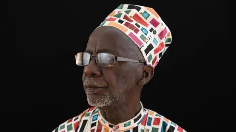 Malian director Souleymane Cissé, wearing glasses and a coloured cap.