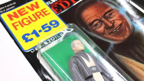 Hansons Auctioneers An Anakin Skywalker figurine, in a box, with a price tag above, with an image from the film to the right.
