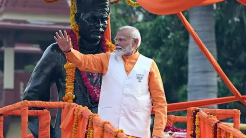 Getty Images Narendra Modi, perdana menteri India, mengenakan jaket putih dengan kemeja oranye dan lencana teratai menyapa para pendukungnya saat kampanye di Varanasi, Uttar Pradesh, India, pada Senin, 13 Mei 2024