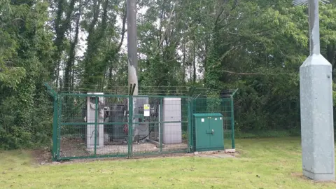 A mast behind green fences.