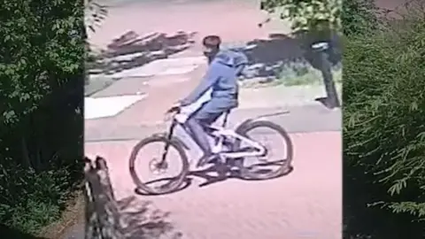 West Yorkshire Police CCTV image showing a teenager on a bike in a street, wearing a mask on his face.