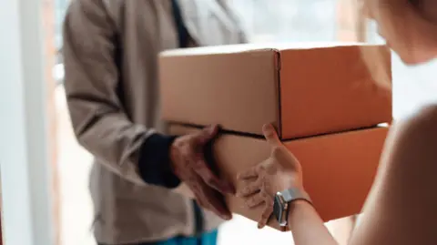 Cropped shot of courier person standing at front door, handing over a parcel to customer