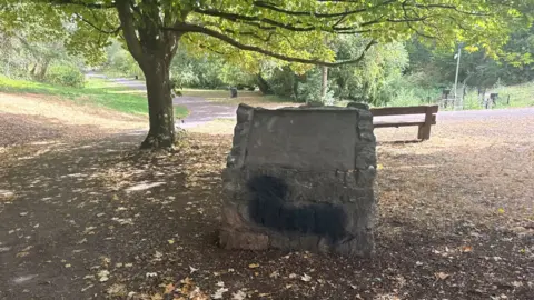This picture was taken in a park. A large piece of stone has a black patch on it where the council sprayed over the an offensive slur. 