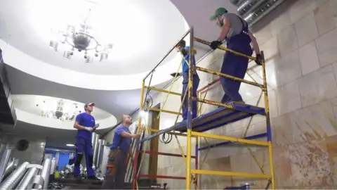 Handout Workers in blue overalls stand on scaffolding in a metro station in Kharkiv