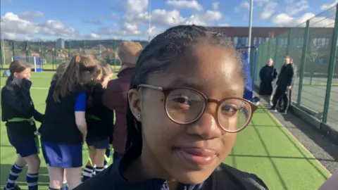 Iwinosa with dark brown hair and glasses on sports pitch.