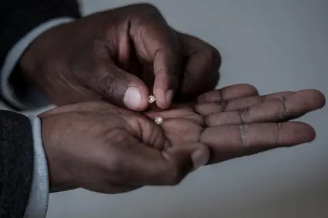 AFP A man holds rough diamonds found by former illegal, now independent, miners, on June 5, 2018 in Kimberly, Northern Cape, South Africa. Unlike formal mining operations, small-scale miners pan for precious minerals around the edge of established quarries in the hope of coming up lucky. In April, some 800 illicit miners received licences to operate on a vast tract of land near Kimberley in the country"s centre. The landmark deal was aimed at curbing the rapid growth of illegal mining which has been spurred on by rising unemployment.