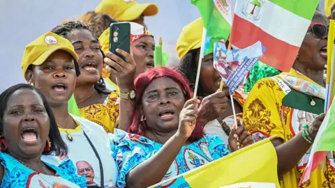 AFP via Getty Images A crowd of women waving flags and wearing clothes with the Pope's face emblazoned on them