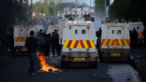 Reuters Shows a petrol bomb in flames beside police Land Rovers 