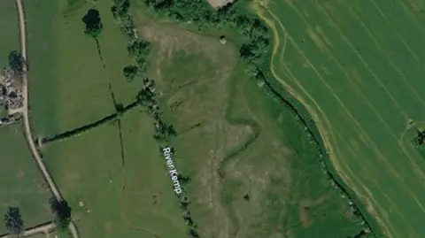 Google A satellite image showing the River Kemp from above, surrounded by bright green fields. On the right, you can see the indent of the river's natural meander etched into the field. 