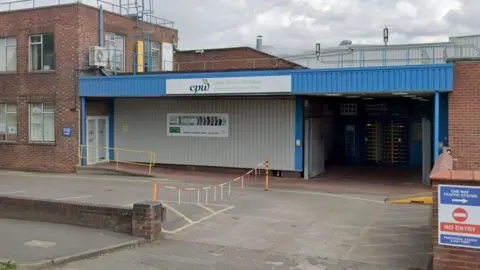 An outside view of a factory building with a a blue entrance and a small car-park