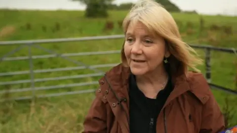 Deb McAndrew wearing a brown coat outside near grass