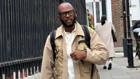 Christopher Joell-Deshields walking down the street in a beige coat and black rucksack.