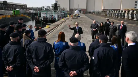 PA Media Prime Minister Sir Kier Starmer addresses submarine crew and others outside a building at BAE Systems in Barrow. Behind him is construction work on a submarine.