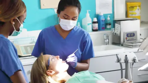 Young female dentist and assistant working on female patient in chair