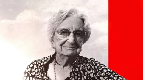 An elderly woman wearing a flowery top looks at the camera