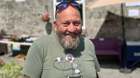 Man with a long beard and moustache and wearing sunglasses on his head smiling at the camera.
