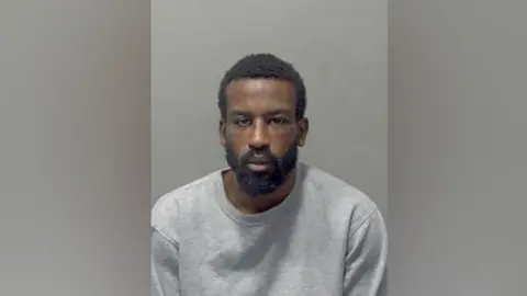 Nathaniel Sereaton: A man with black hair and a black beard wear a grey, round-necked T-shirt