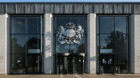 Getty Images The outside of Coventry Crown Court, a glass-fronted building with grey stone pillars separated by large panels of glass. In the middle are two revolving doors and above them, the British coat of arms with a lion on one side of a shield, a unicorn on the right.