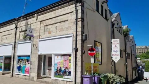 The former Waterloo Inn pub in Bangor, which has boarded up white windows with adverts. The whole building is made of pale stone 