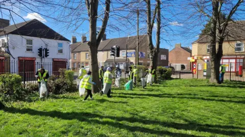 Peterborough Litter Wombles People in green high-visibility jackets, litter picking on the grass.