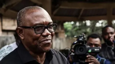 Getty Images Peter Obi wearing glasses and a dark shirt. Two photographers can be seen behind him