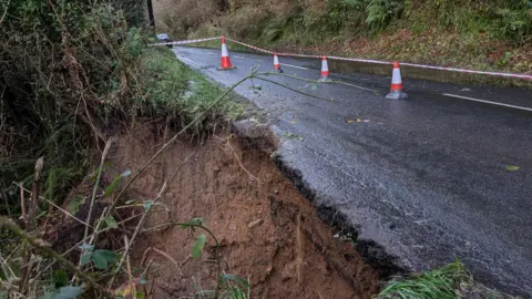 Kevin McCaughan A landslide on the Glenshesk Road following Storm Bert.  A section of the roadside verge has fallen down a hill.  The section of road has been cordoned off with traffic cones and plastic tape.  