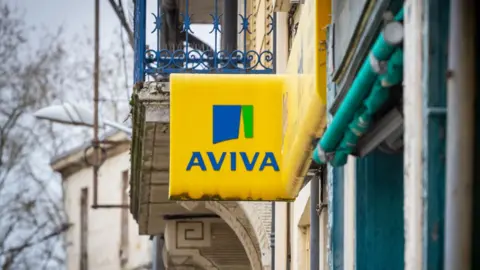A yellow Aviva signs hangs outside a building on a grey skied day