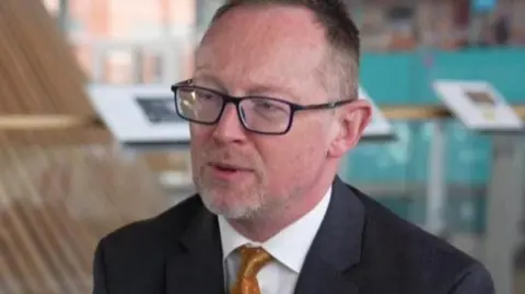 BBC Russell George sat on a chair in front of the funnel at the centre of the Senedd building in Cardiff Bay.