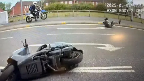 Durham Police A moped lies on its side in the middle of the road. A teenager lies on his back with his legs in the air at the other side of the asphalt. An off-road motorbike and its rider stand on the far pavement, near the person on the ground.