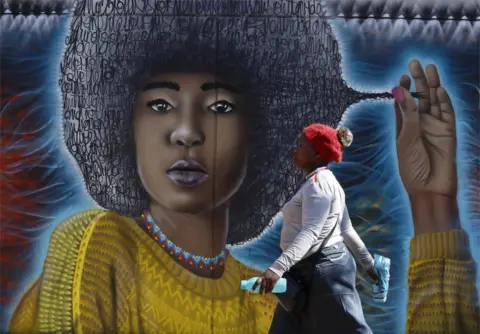 EPA A woman walks past a spray-painted mural depicting a woman with an afro.