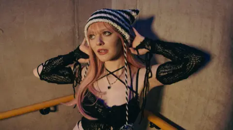 Woman wearing a black and white hat against a stone wall with a bannister 