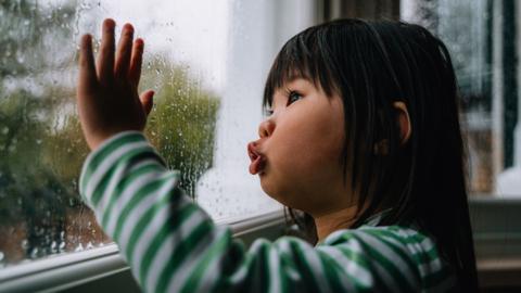 Young girl looking out the window which has rain droplets on