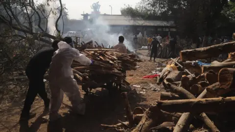 Getty Images Relatives carry firewood for use in funeral pyres