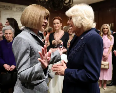 Pool via Reuters Anna Wintour and the Queen gesture while meeting at the library with other guests in the background.