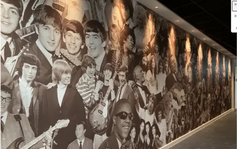 Shaun Whitmore/BBC A mural fills an entire wall creating a collage of black and white headshots and and head and shoulders images of performers, including The Rolling Stones, The Beatles, Stevie Wonder, Buddy Holly, Jimi Hendrix and Dolly Parton