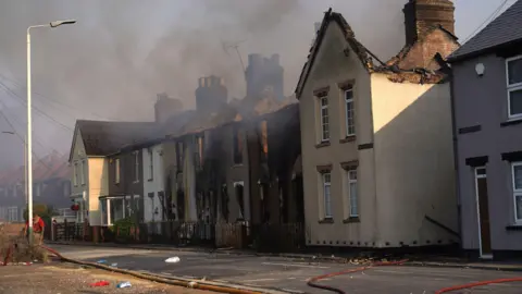 PA Media A row of houses on a residential street, many of them burned out.