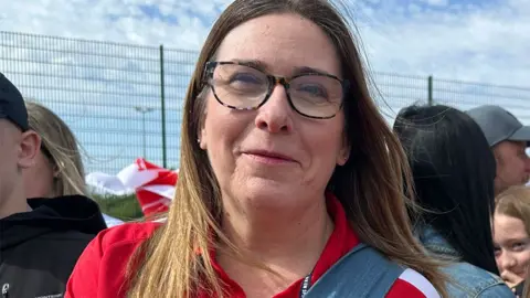 Matt Dean/BBC Sarah Clark has long brown hair and is wearing glasses and a Hull KR red shirt 