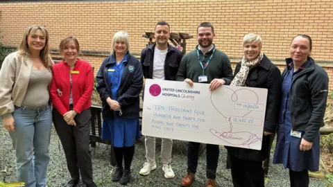 A group of people, including nursing staff, standing in line. Two of the people are holding a giant cheque.