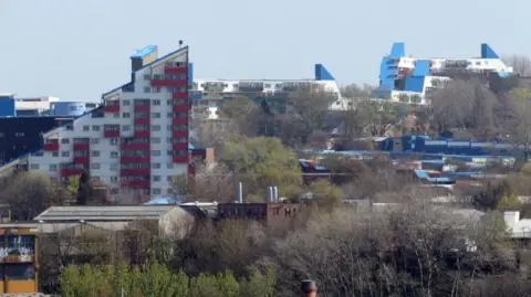 The Byker Wall in Newcastle. The white and red building his triangular in shape with a jagged roof. The windows of the apartments can be seen.