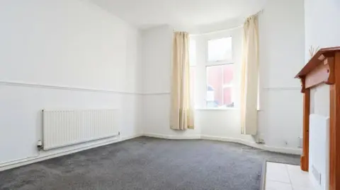 Chris Davies Estate Agents Living room with radiator on the left, window in the centre, and boarded up fireplace on the right