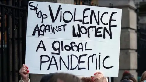 PA Media A woman holding up a homemade sign at a protest which says "Stop violence against women. A global pandemic."