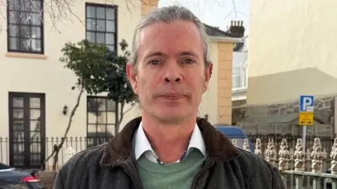 A man wearing a shirt, jumper and jacket